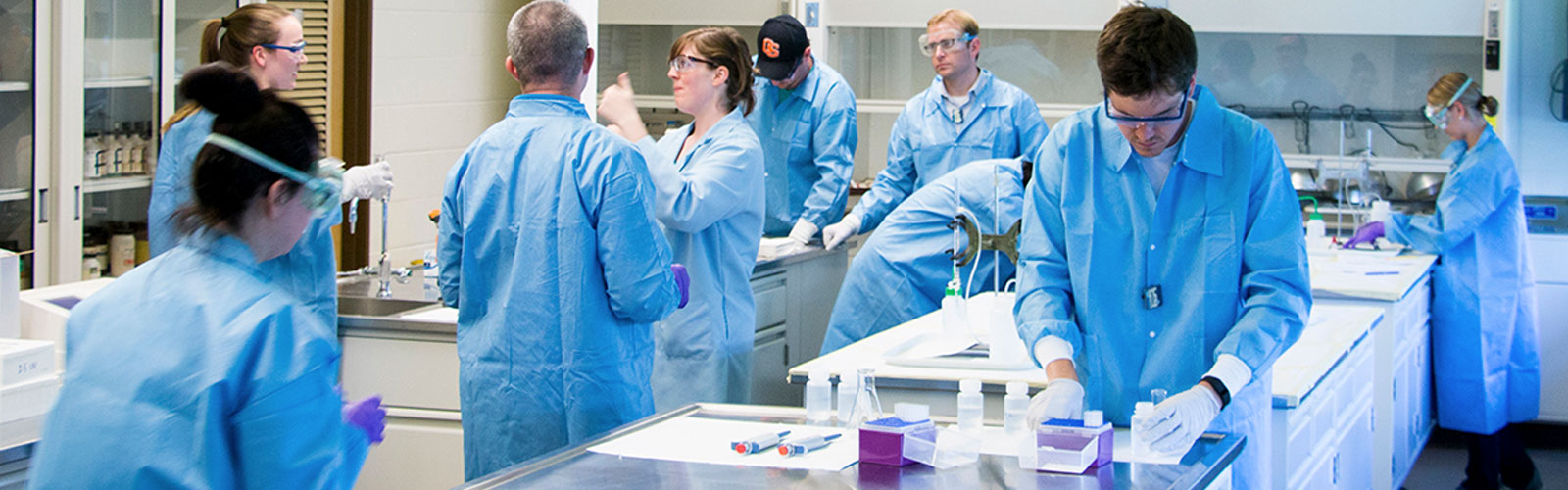 laboratory full of students in blue lab coats working on experiments